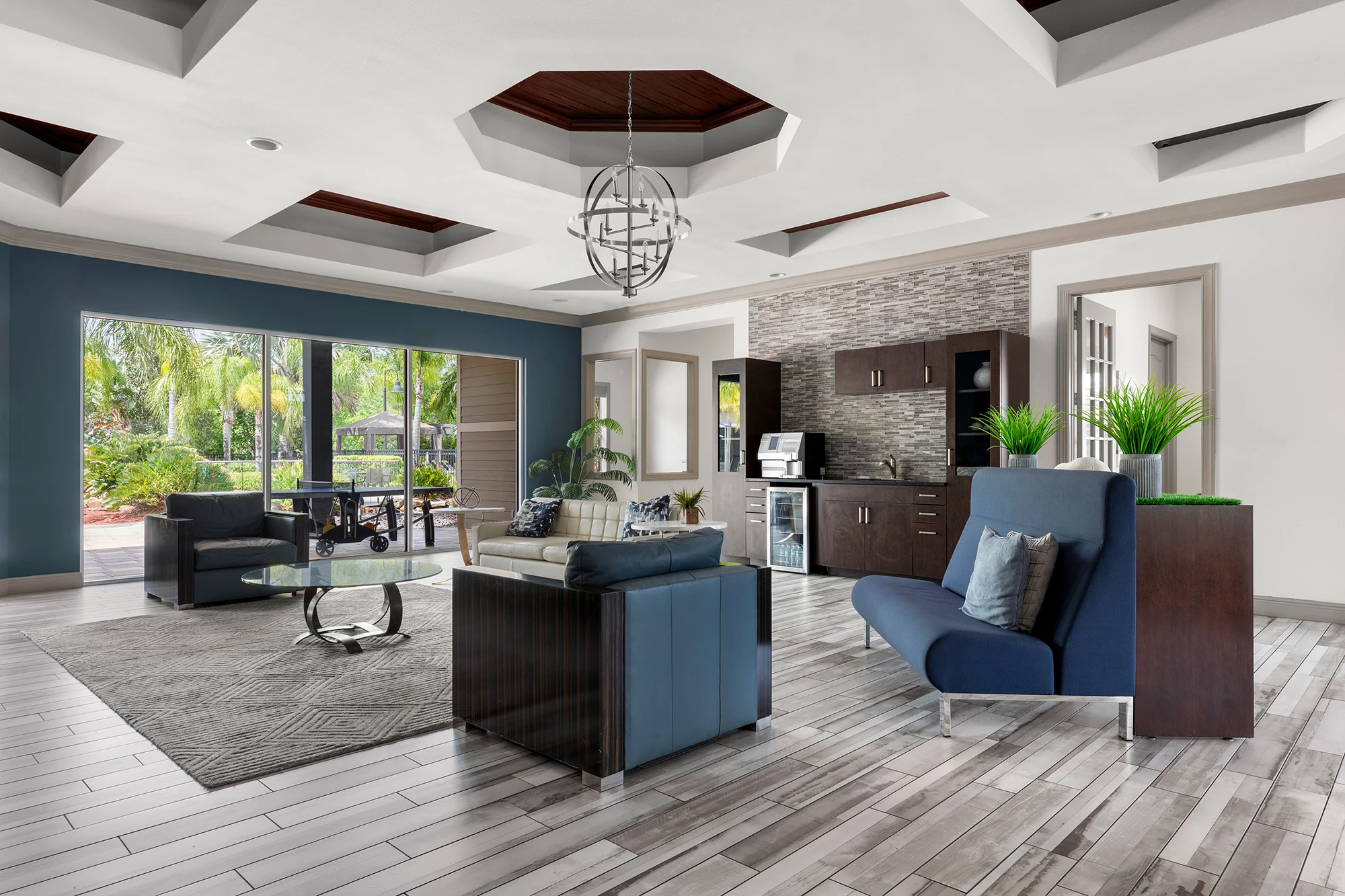 Sitting area with blue arm chair and couches with greenery in the windows.